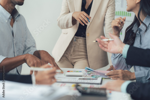 Collaborative Business Meeting: A diverse group of professionals engages in a focused discussion around a table strewn with charts and reports.