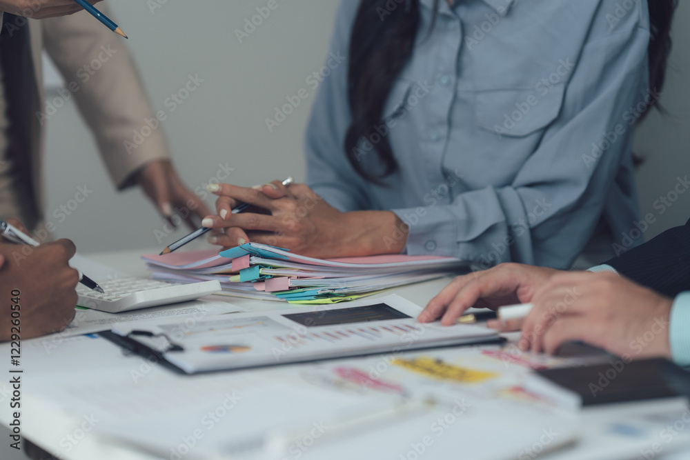 Strategic Business Meeting: A diverse team of professionals engages in a collaborative discussion around a table, reviewing financial documents and charts.