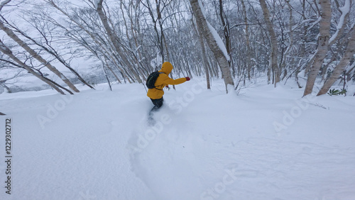 Unrecognizable active male tourist snowboards fresh powder off piste in the picturesque wintry Rusutsu forest. Following extreme freeride snowboarder shredding fresh pow in the Japanese backcountry photo