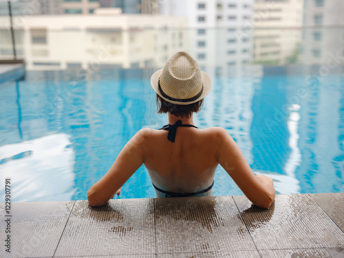 Photography Young asian woman relaxing by pool at Kuala Lumpur hotel with view of surrounding skyscrapers, enjoying leisure time in vibrant urban setting