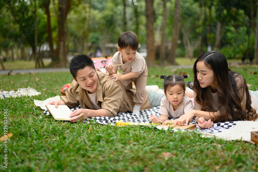 Fototapeta premium Happy family lying together on a picnic blanket. Parenting, family, and outdoor leisure concept