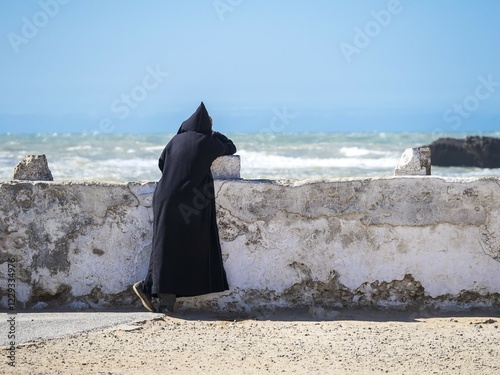 A Berber with black djellaba leaning against the harbor wall, Place Moulay Hassan, Essaouira, Morocco, Africa
