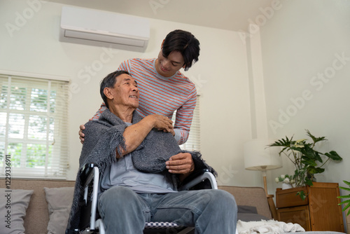 Son wrapping a warm blanket around elderly father in a wheelchair. photo