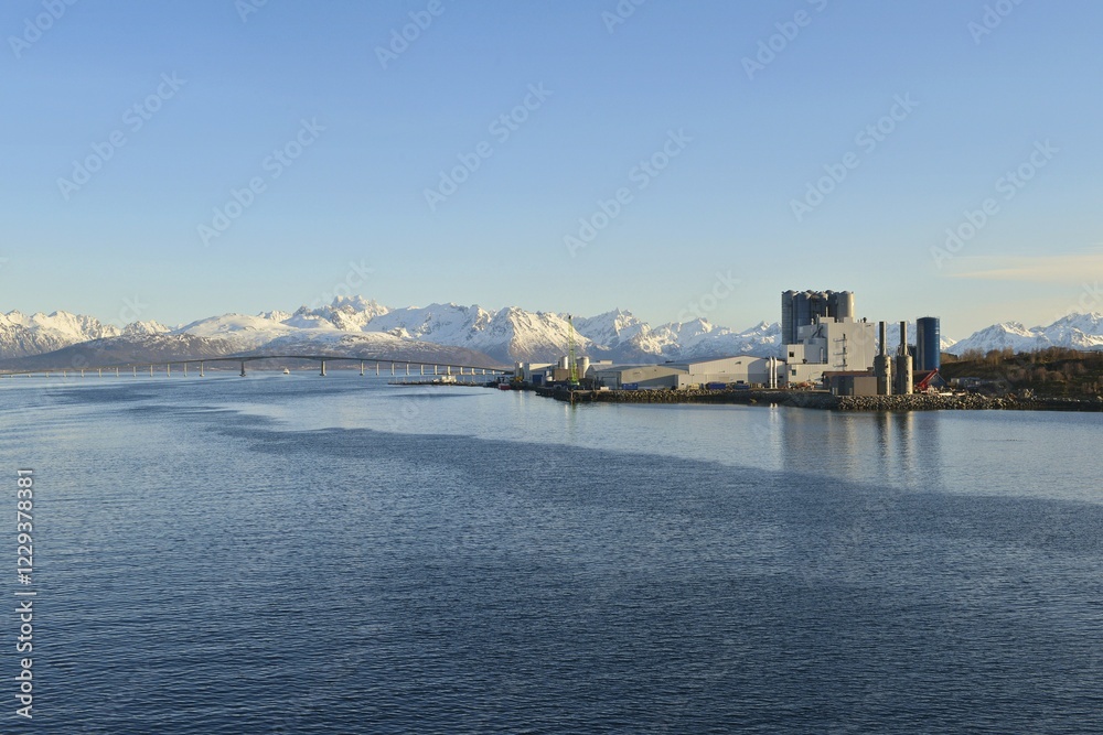 Obraz premium Industrial plant on blue Langøysund, behind the snowy peaks of Hinnøya Stokmarknes, Nordland, Vesteralen, Norway, Europe