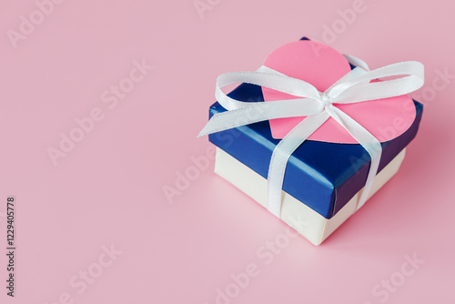 A blue gift box with a pink heart on the lid, tied with a white ribbon with a bow. Valentine's Day gift concept.