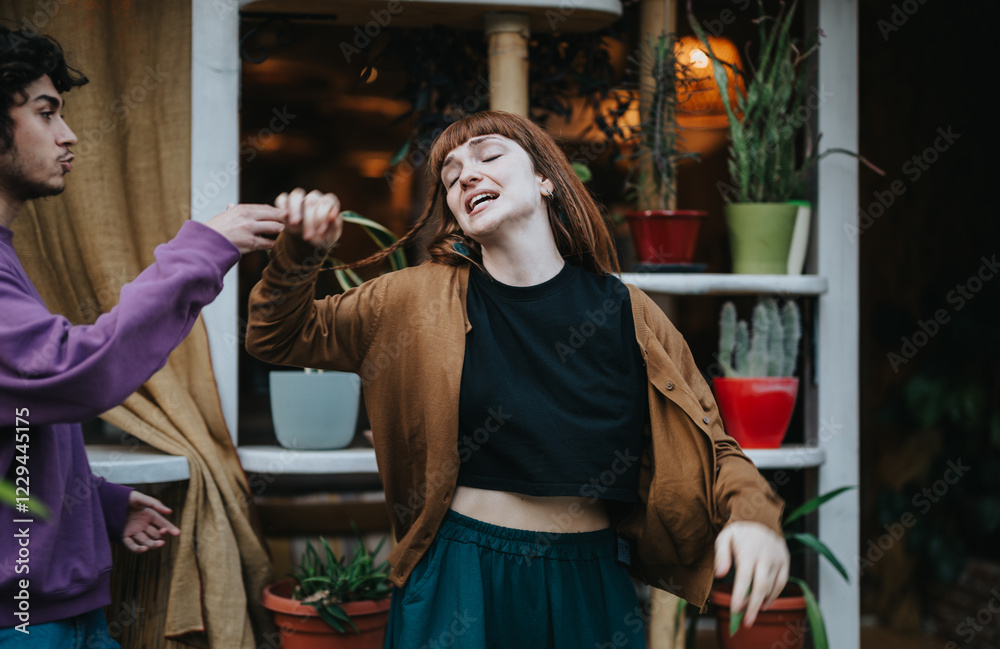 Obraz premium A young couple shares a joyful moment, dancing playfully in a cozy setting surrounded by plants. The image captures a sense of carefree happiness and connection.