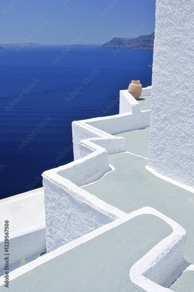 Fototapeta premium Angled terrace with a gray floor and white walls, yellow clay vase, in front of the blue sea, Oia, Ia, Santorini, Cyclades, Greece, Europe