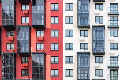 Contemporary apartment buildings with beige and red facades, featuring numerous balconies with dark-framed windows. Urban housing concept, front view