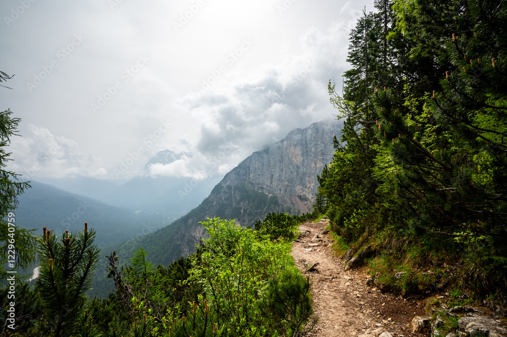 Mountain trail in the Dolomites (Dolomiti, Dolomiten), Italy, leading to Lago Sorapis. The path winds along rocky slopes with stunning views of valleys, forests, and peaks