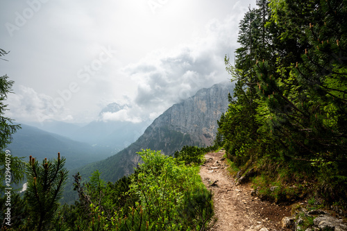 Mountain trail in the Dolomites (Dolomiti, Dolomiten), Italy, leading to Lago Sorapis. The path winds along rocky slopes with stunning views of valleys, forests, and peaks