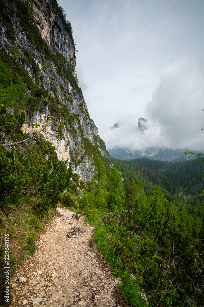Mountain trail in the Dolomites (Dolomiti, Dolomiten), Italy, leading to Lago Sorapis. The path winds along rocky slopes with stunning views of valleys, forests, and peaks