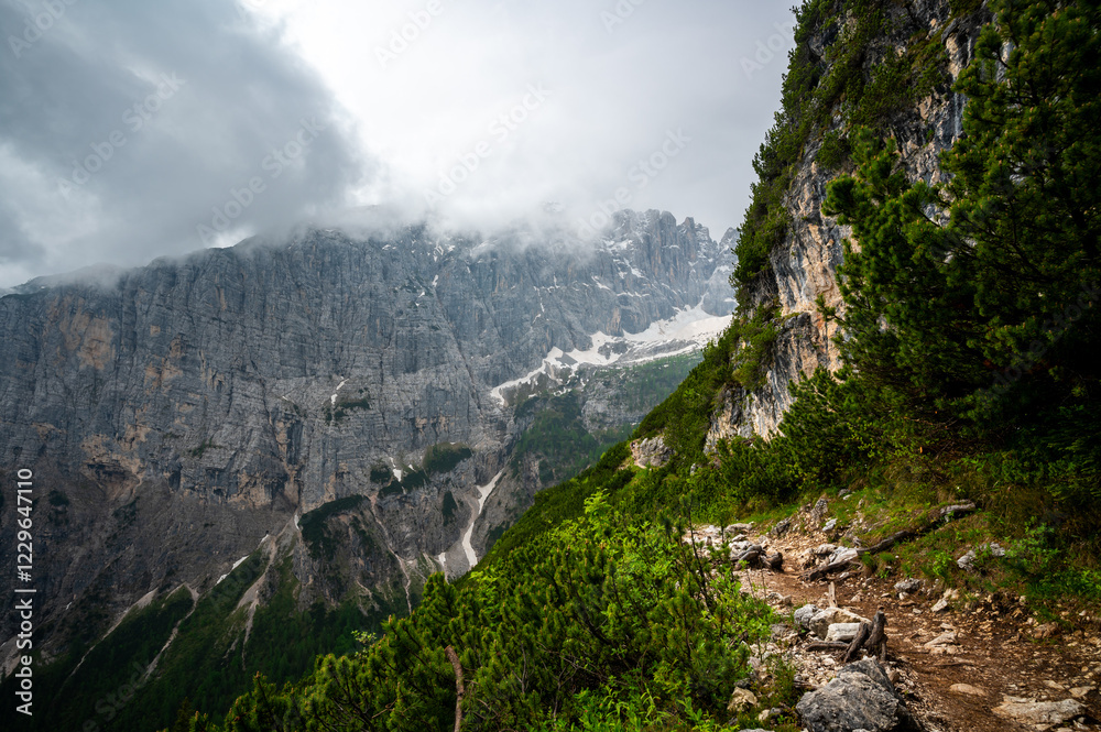 Mountain trail in the Dolomites (Dolomiti, Dolomiten), Italy, leading to Lago Sorapis. The path winds along rocky slopes with stunning views of valleys, forests, and peaks
