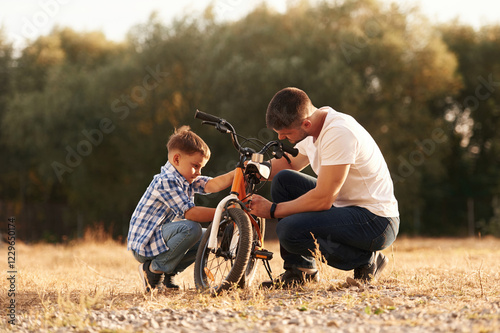 Broken bike, process of fixing it. Dad with son are with bicycle on the field outdoors