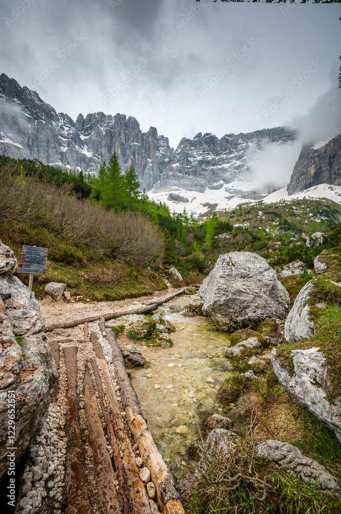 Rocky hiking trail near Lago Sorapis in the Dolomites (Dolomiti, Dolomiten), Italy. The path runs alongside a small mountain stream, with massive boulders and peaks in the background