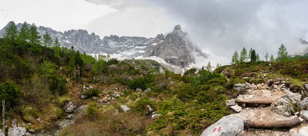 Rocky hiking trail near Lago Sorapis in the Dolomites (Dolomiti, Dolomiten), Italy. The path runs alongside a small mountain stream, with massive boulders and peaks in the background