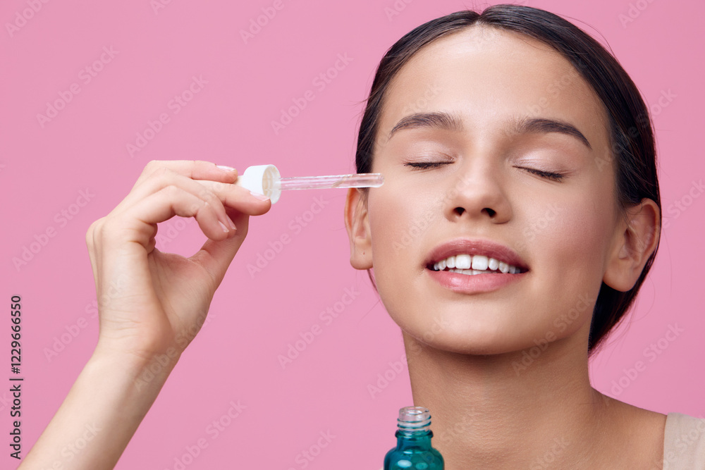 Young woman applying facial serum with dropper, showcasing a glowing complexion against a soft pink background, emphasizing skincare and self care routine Young woman applying facial serum with dropper, showcasing a glowing complexion against a soft pink background, emphasizing skincare and self care routine