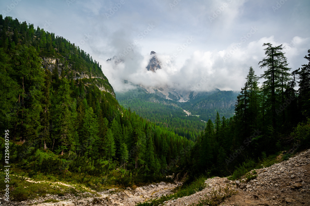 Mountain trail in the Dolomites (Dolomiti, Dolomiten), Italy, leading to Lago Sorapis. The path winds along rocky slopes with stunning views of valleys, forests, and peaks
