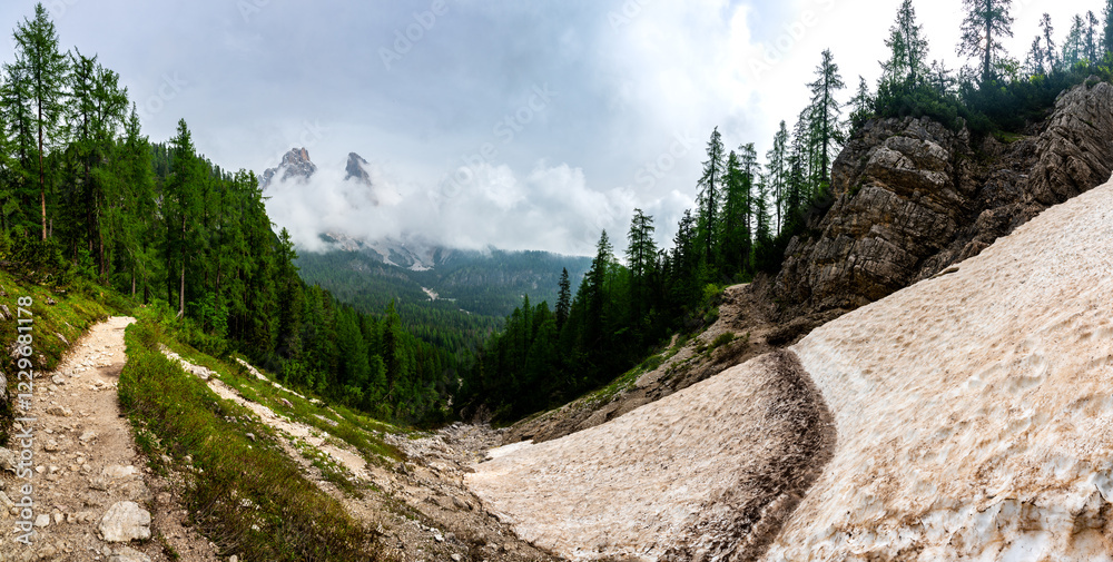 Mountain trail in the Dolomites (Dolomiti, Dolomiten), Italy, leading to Lago Sorapis. The path winds along rocky slopes with stunning views of valleys, forests, and peaks