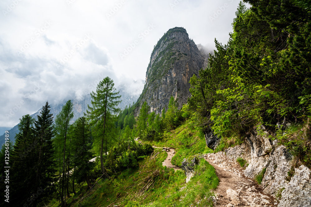 Mountain trail in the Dolomites (Dolomiti, Dolomiten), Italy, leading to Lago Sorapis. The path winds along rocky slopes with stunning views of valleys, forests, and peaks