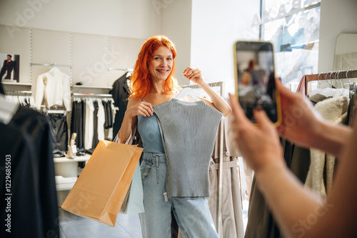 Making a photo by using smartphone. Two female friends are in the retail store, choosing clothes, shopping photo