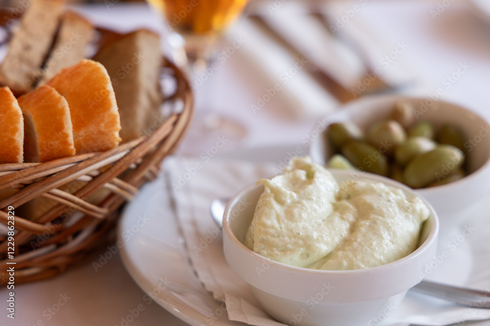 Traditional Mediterranean aioli served as an appetizer with fresh bread slices in a woven basket and a side of marinated green olives on a dining table setting Traditional Mediterranean aioli served as an appetizer with fresh bread slices in a woven basket and a side of marinated green olives on a dining table setting