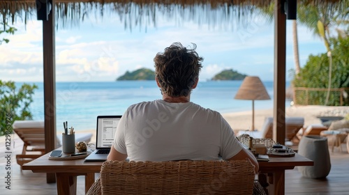 A person sits at a wooden table with a laptop, gazing at a serene beach view, surrounded by tropical decor and nature.