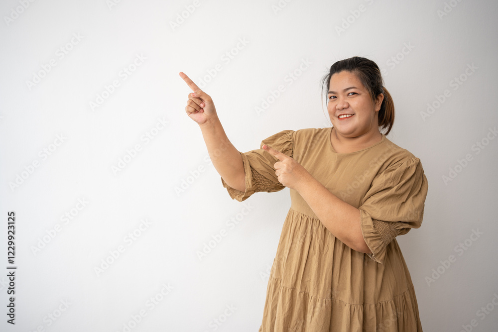 Smiling Woman Pointing: A plus-size woman in a beige dress beams radiantly, her index fingers playfully pointing towards a space to the side, creating a vibrant and engaging image. Smiling Woman Pointing: A plus-size woman in a beige dress beams radiantly, her index fingers playfully pointing towards a space to the side, creating a vibrant and engaging image.