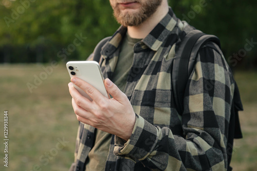 A man in a green shirt uses a white smartphone on a blurred background of nature outside, technology use concept, copy space. photo