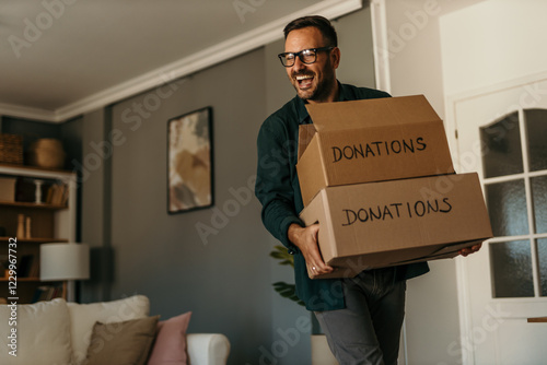 A smiling man is carrying boxes for donations in his bright living room. Copy space