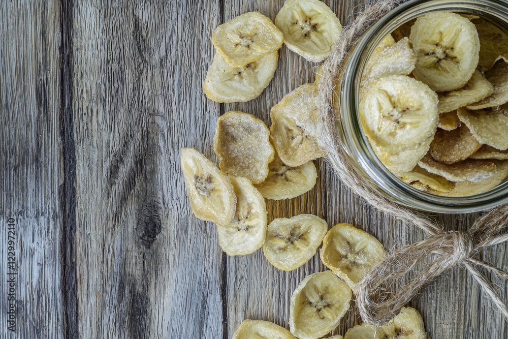 Fototapeta premium Banana Chips in a Glass Jar Light, crunchy banana chips with a golden hue, showcased in a jar tied with a rustic ribbon