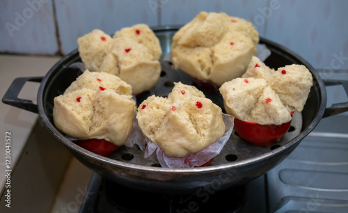 Steaming basket with Huat Kueh (Chinese prosperity cakes). Light yellow, split-top cakes with red dots, nestled on paper liners.  Ready for serving. Blue patterned background.