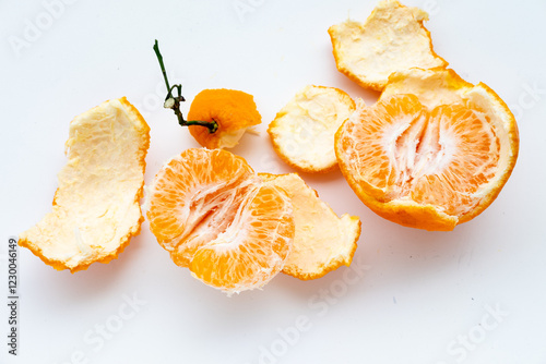 A partially peeled mandarin orange with segments exposed, alongside peel pieces and a whole fruit with stem, on a white background.