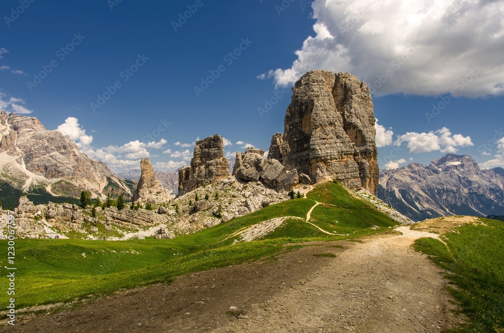 Obraz premium Majestic Cinque Torri in Dolomie Alps during day. Stunning view on Five Towers group, with blue sky and clouds and foot road. Amazing nature lanscape. Mountain trail leading along the mountain ridge.