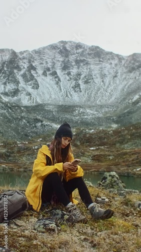 Vertical video. Happy hiker taking selfie with smartphone in mountain landscape with lake and snowy peaks, enjoying freedom and adventure in nature during trekking trip