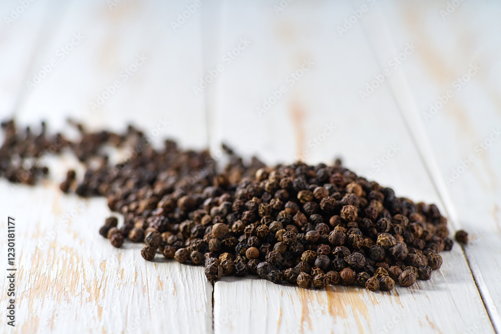 Heap black pepper seeds on a white wooden table, selective focus. Heap black pepper seeds on a white wooden table, selective focus.