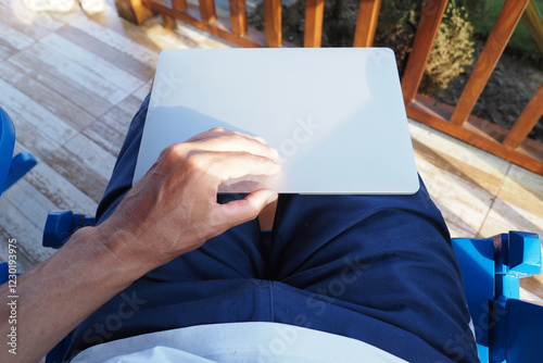 Personal perspective. A person sits comfortably in a blue chair outdoors, using a laptop placed on their lap.