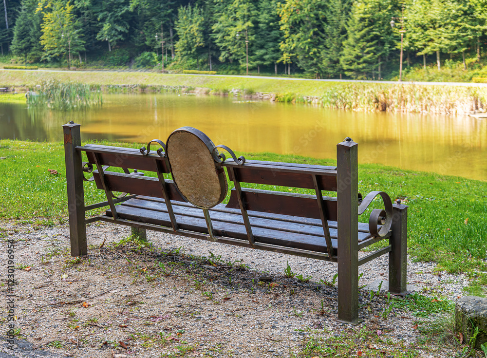 Bench with an artistic round stone element in its backrest, situated by a peaceful lake surrounded by lush greenery.