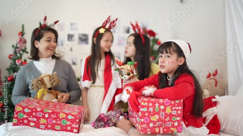 Joyful family dressed in festive costumes enjoying Christmas together on a bed, surrounded by gifts and decorations in a cozy, cheerful holiday atmosphere.