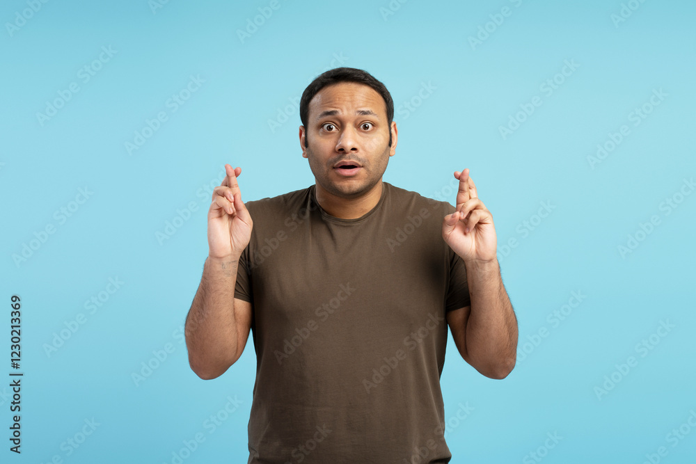 Fototapeta premium Hopeful man crossing fingers wishing for good luck on blue background