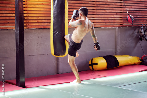 Tattooed athlete practicing kickboxing with punching bag photo