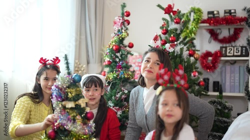 Mother and daughters joyfully decorating a Christmas tree at home, celebrating the holiday season with ornaments, costumes, and festive spirit.