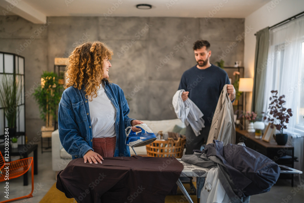 Fototapeta premium A woman iron shirts on an ironing board, while a man folds up them