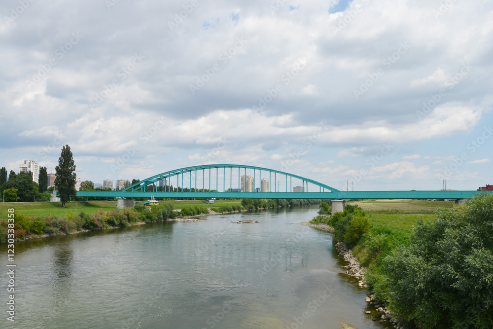 Naklejka premium A scenic view of the Green Railway Bridge, also known as Hendrix Bridge, spans the Sava River in Zagreb, Croatia, under a partly cloudy sky