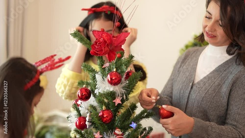 Mother and daughters joyfully decorating a Christmas tree at home, celebrating the holiday season with ornaments, costumes, and festive spirit.