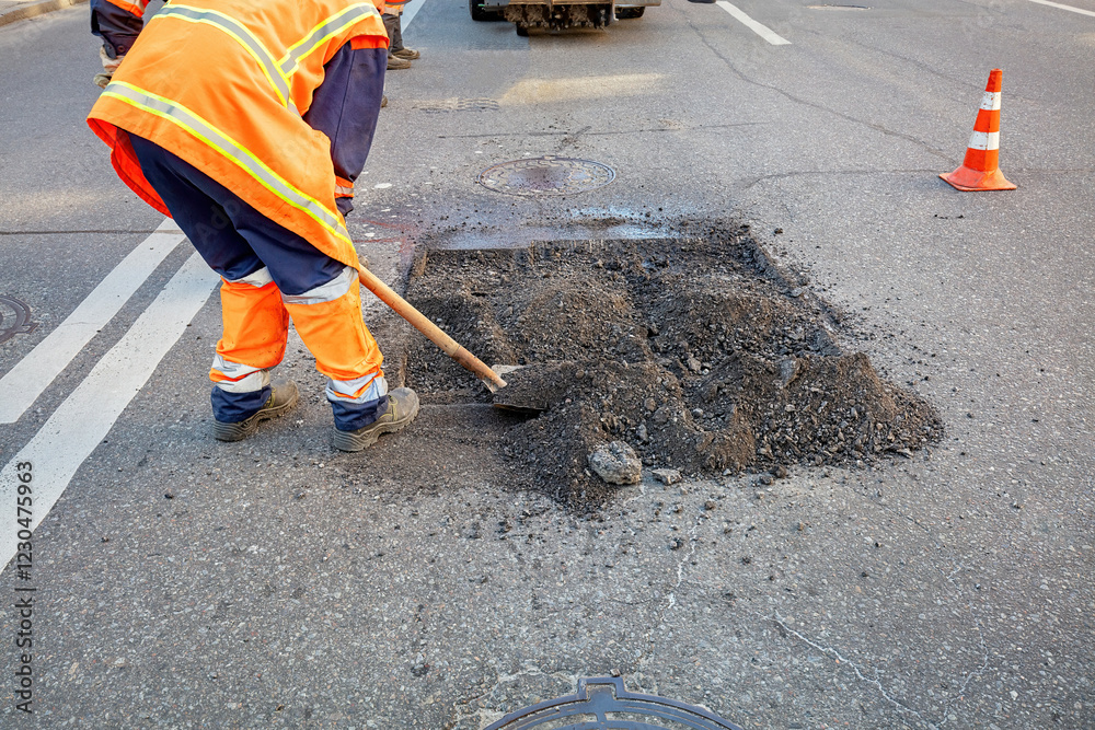Road workers repair pothole in bright orange uniforms on a busy street. Copy space.