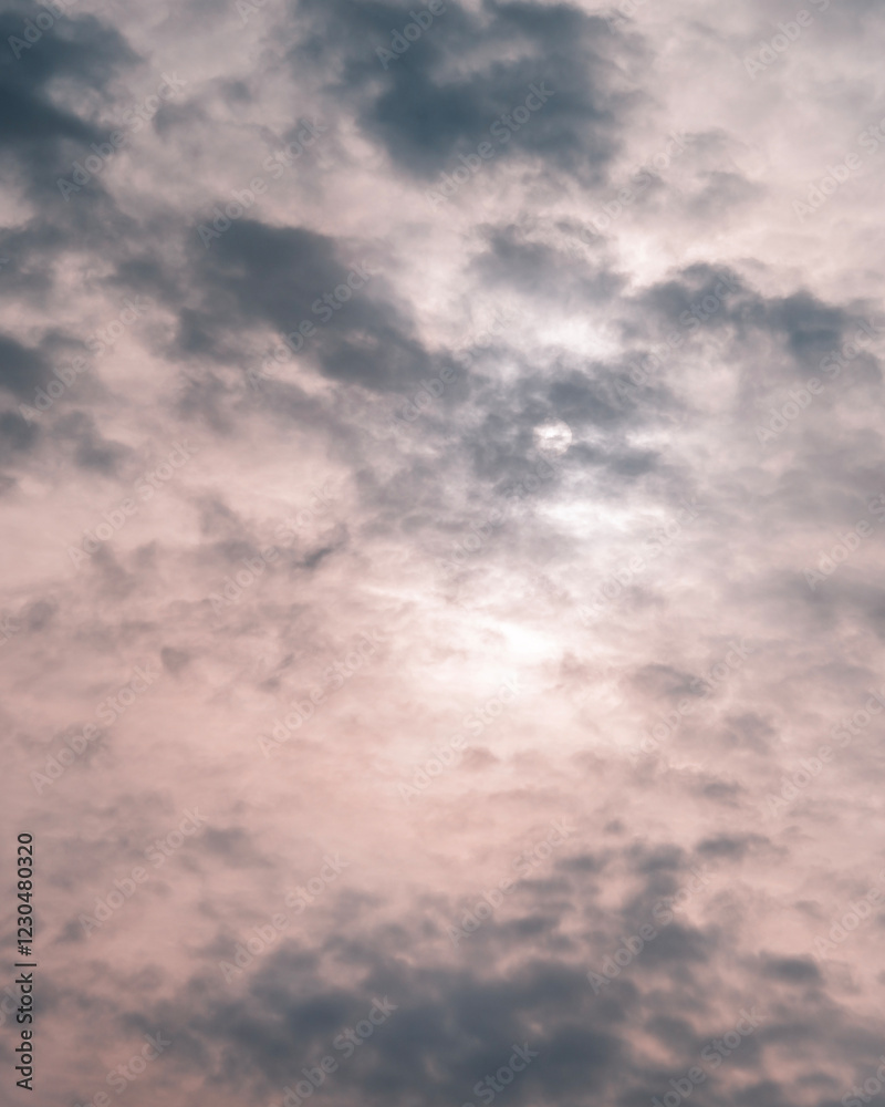 Dramatic clouds in soft pastel shades of pink and gray partially cover the sun, creating a moody sky background. Atmospheric and minimalistic.