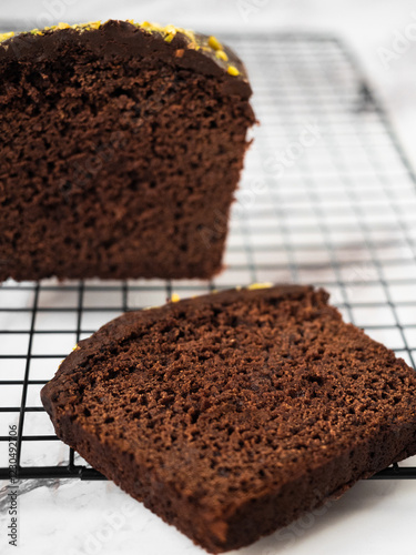 Sliced cake on a cooling rack with a bigger cake on the side. White marble counter as a background