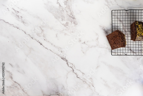 Sliced cake on a cooling rack with a bigger cake on the side. White marble counter as a background