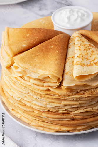 Stack of traditional russian pancakes blini with sour cream on marble background