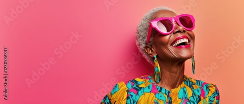Cheerful senior Black woman with pink sunglasses and colorful top laughing joyfully against a vibrant pink and orange background Concept of happiness, fashion, and positive aging